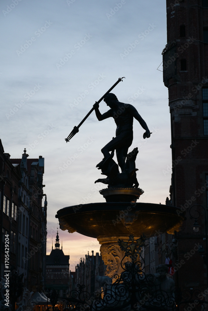Obraz premium Neptune's Fountain at night, historic fountain in Gdansk, Poland. One of the most known landmarks of the city. View with city buildings in the background.