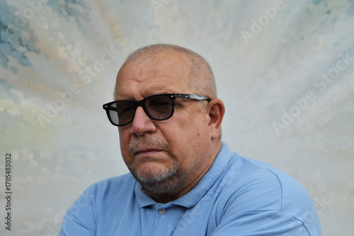 Caucasian mature man with beard wearing sunglasses and blue polo shirt with serious expression.