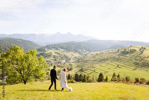 Wallpaper Mural A happy married couple with a cute white dog walking through a lush green meadow. A beautiful woman and man enjoying the weather and time together with their pet. Love and family concept. Torontodigital.ca