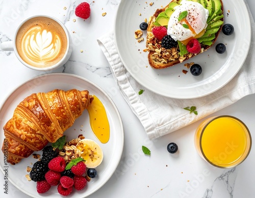 Delicious breakfast spread with croissant, avocado toast, poached egg, fresh berries, coffee, and orange juice on marble.