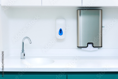 Sterile sink area with faucet, soap dispenser, and stainless steel paper towel holder in medical facility