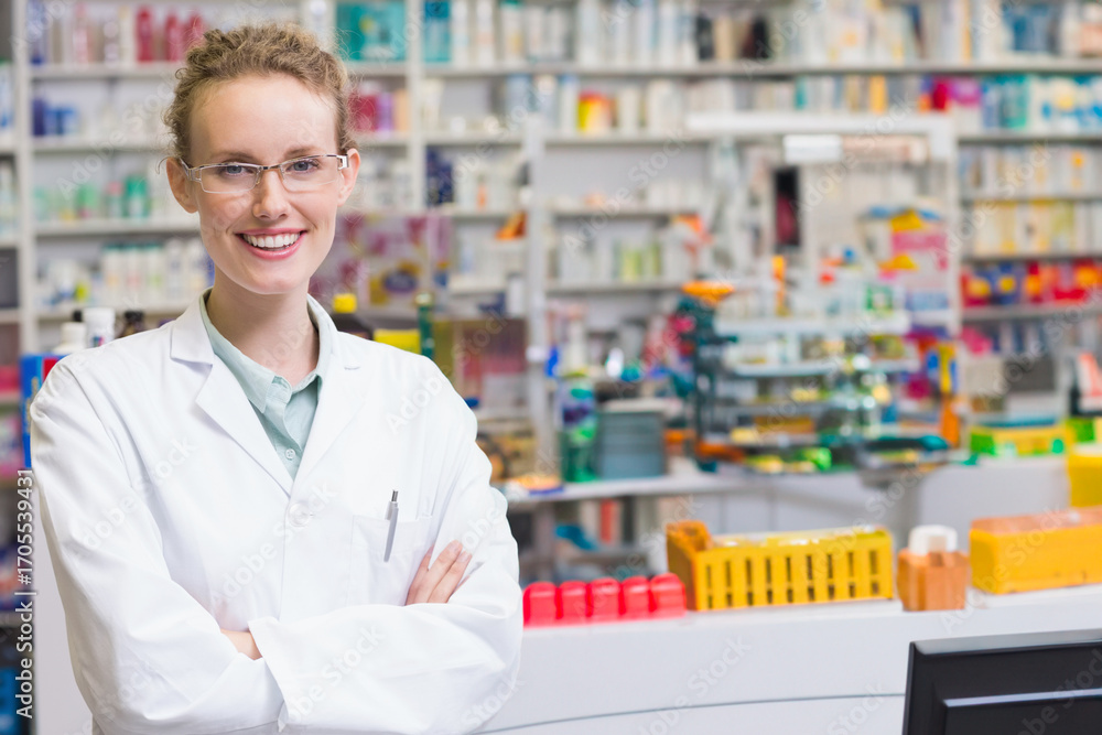Female pharmacist wearing coat using dispensing trays and monitor at pharmacy counter, copy space