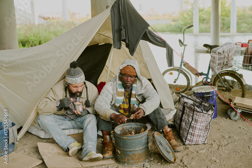 Bild auf Leinwand Middle aged Asian man and middle aged Black man sitting on ground under bridge n