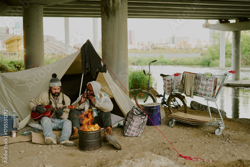 Bild auf Leinwand Two middle aged men, one Caucasian and one Black, sitting by campfire under brid