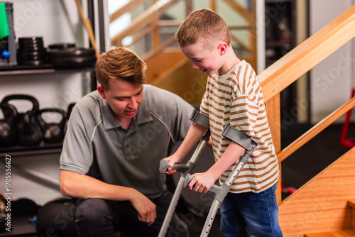 Trainee physiotherapist student teaching young boy how to walk with and use crutches