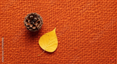 A top-down view of a pinecone and a single yellow leaf resting on a textured burnt orange fabric background