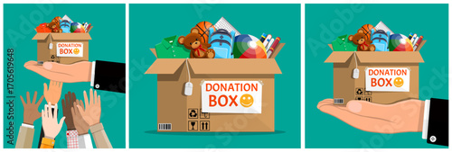 Man hands holding donation box with clothes, toys, books, and school supplies for charity. Volunteering and social assistance concept.