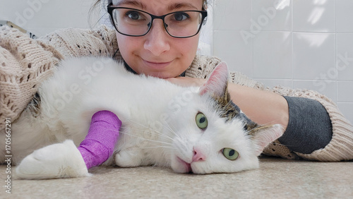 White kitty with wrapped paw having a selfie with its owner at veterinary office
