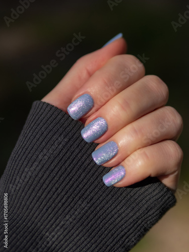 Close-up of Hand with Silver Cat Eye Magnet And Pink Shimmer Nail Polish. Nail Lacquer Swatch. Periwinkle Blue Magnetic Lacquer With Pink Shimmer And Silver Cat Eye Magnet On Fingers. Gray Long Sleeve