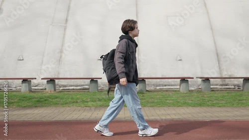 A boy student walks with a backpack, returning from school. The child is on his daily commute through a city park. Education and childhood journey of a lonely kid going back to school.