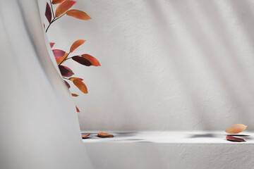 Autumn background with falling leaves on white table with sunlight. Minimal interior showroom for luxury beauty and cosmetic product placement mockup. Fall season and thanksgiving holiday design.