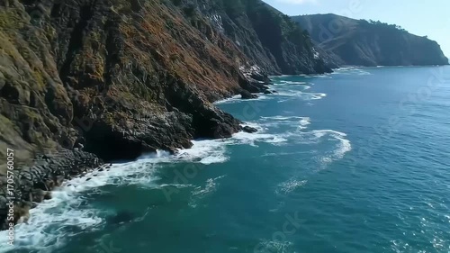 Coastal cliffs meet the ocean, with waves crashing against the rocky shore.