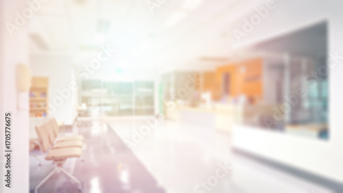 Blur abstract background of corridor in clean hospital. Blurry view of aisle in office with light floor. Defocus walkway in white light building hall with patient registration at reception desk.