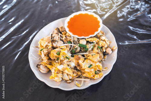 Thai street food. Oyster Omelet fried with Rice flour, tapioca flour bean sprout and sprinkled with chopped green onions ground pepper served with chili sauce Place on table and eat simply.