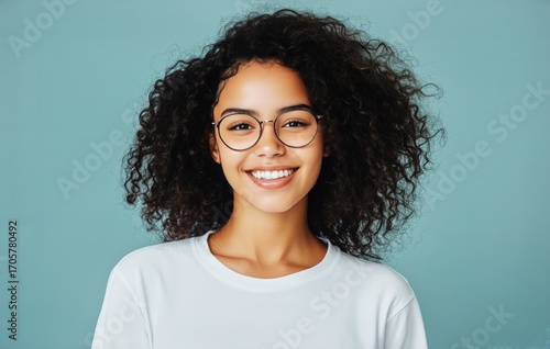 Smiling Young Woman With Curly Hair and Glasses Against a Teal Background.