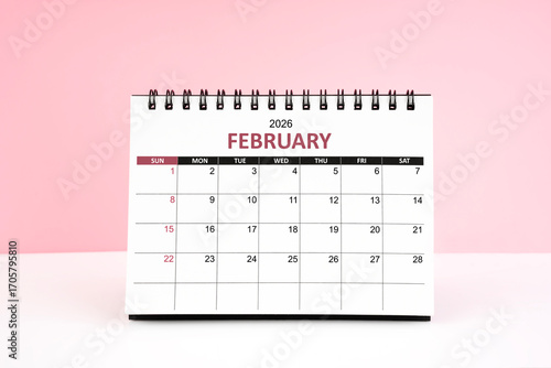 February 2026 desk calendar on white table with pink color background.