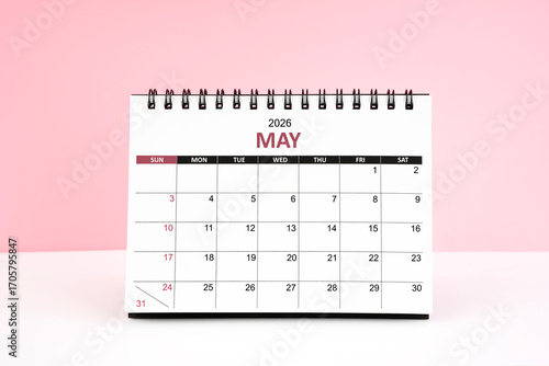 May 2026 desk calendar on white table with pink color background.