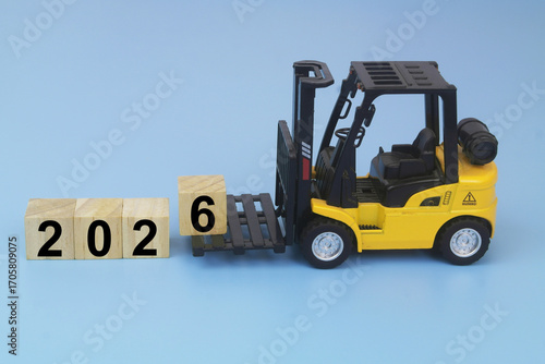 Yellow forklift truck arranging cubes with numbers 2026 on blue background. Symbol of new year coming.