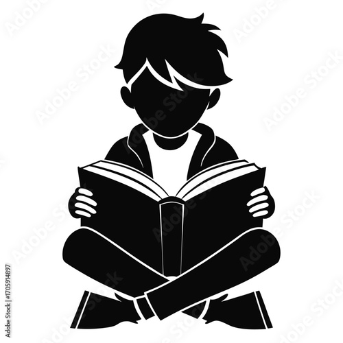 Silhouette of a young boy sitting crosslegged and attentively reading an open book