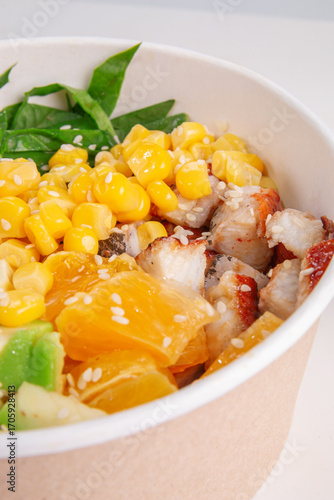 Close up of healthy chicken poke bowl with sweet corn, juicy orange slices, avocado, greens and sesame seeds in eco paper bowl, macro food photography