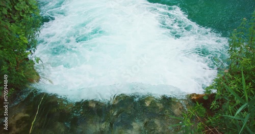 White foamy water rushes over the edge of a waterfall into a turquoise pool at Plitvice Lakes National Park Croatia