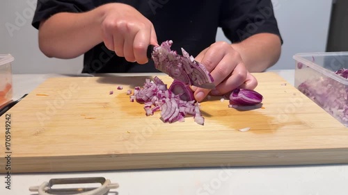 Woman skillfully chops red onion on wooden cutting board, using sharp knife for culinary dish preparation