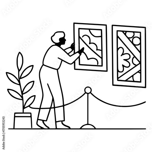 Artist carefully arranging art in a gallery space with plant and rope barriers, ready for display