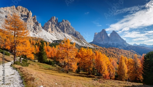A Majestic Autumn Landscape Featuring The Dolomites Characterized By Imposing Rocky Peaks And A Clear Blue Sky With Scattered Clouds The Foreground Is Filled With Vibrant Orange Larch Trees Contras