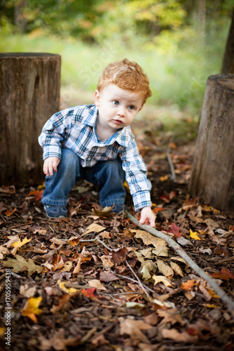 Little Toddler Boy Picking Up a Stick While Exploring Woods