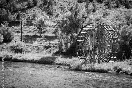 Canvastavla Black-and-white scenic view of a rustic historic water wheel beside a flowing river, framed by trees and rugged hillside — timeless rural landscape