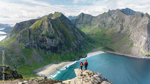 Tableau sur toile Two hikers admire the stunning landscape from Ryten peak, gazing at the turquoise waters of Kvalvika Beach