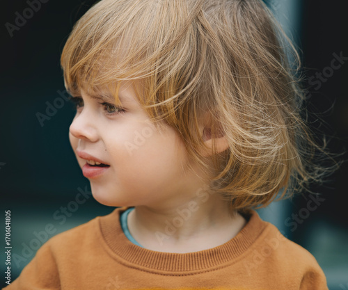 A candid portrait of a curious boy in a natural outdoor setting. The focus is on the child's face and his pensive expression as he looks into the distance.