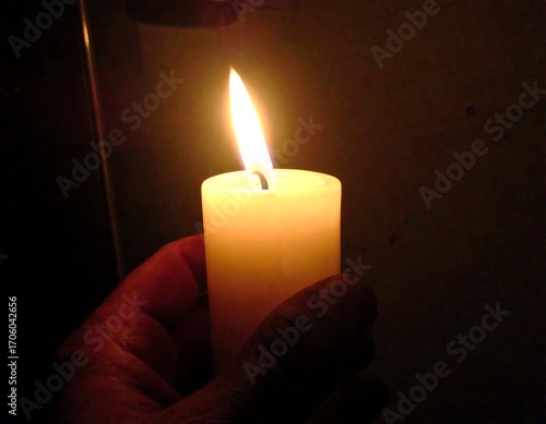 Hand holding a lit candle in darkness