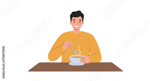 Smiling young man in a yellow sweater enjoying a bowl of hot steaming soup at a table.