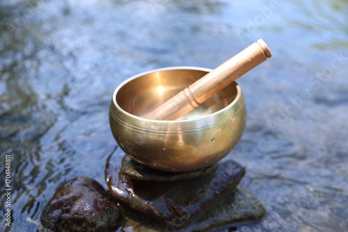 Photography Tibetan singing bowl with mallet on stone near river, closeup