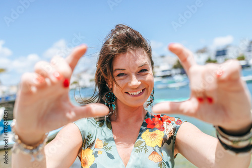 Portrait of a smiling woman making a frame with her hands with boats and the sea in the background