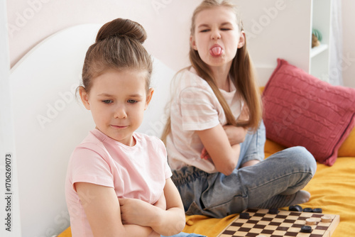 Obraz na plátně Two sisters playing checkers on a bad and having small fight