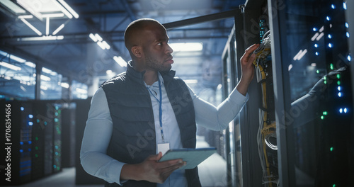 Data center technician inspects server racks, checks network cables.