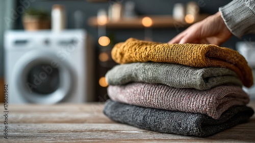 Stack of cozy knitted sweaters on wooden table with washing machine background scene