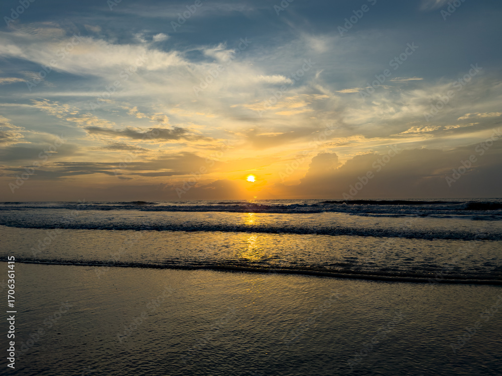Obraz premium Sunrise Over the Ocean with Reflections on Calm Sand