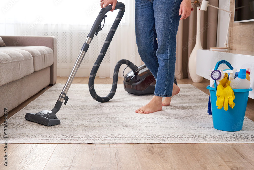 Fototapeta premium Woman cleaning the carpet with vacuum cleaner in the living room