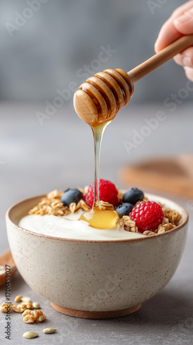 Honey drizzling on yogurt bowl with granola and berries for a healthy breakfast