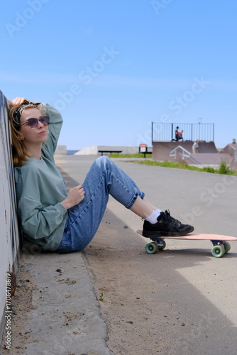 A teenage girl walks in the park with a skateboard. Leisure activities by modern youth