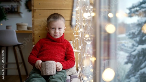 Young child enjoying hot beverage by window on snowy day