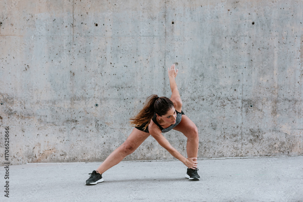 Fototapeta premium Young Hispanic woman stretching and exercising in sportswear outdoors in urban area in Latin America