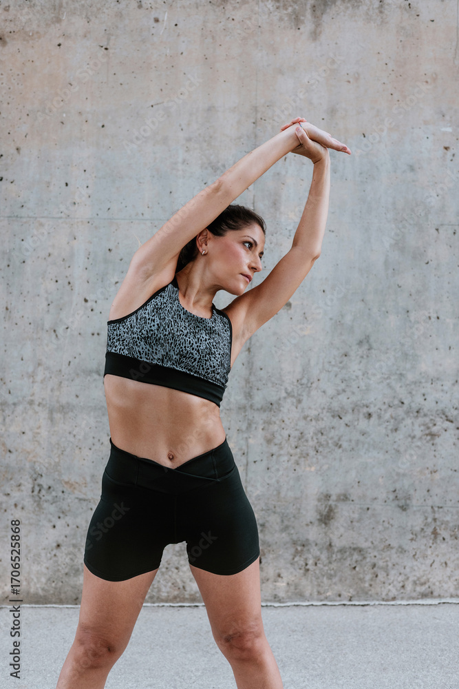 Fototapeta premium Young Hispanic woman stretching and exercising in sportswear outdoors in urban area in Latin America