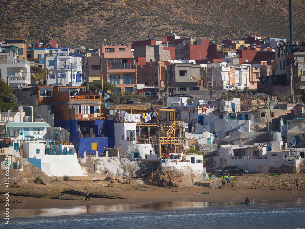 Fototapeta premium CLOSE UP: Scenic coastal town with colorful houses and surfers on the beach. Vibrant blend of modern and traditional architecture in a surfing village overlooking the sandy shore and Atlantic Ocean.