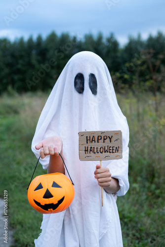 Billede på lærred A child dressed in a ghost costume is joyfully holding a sign that reads Happy Halloween