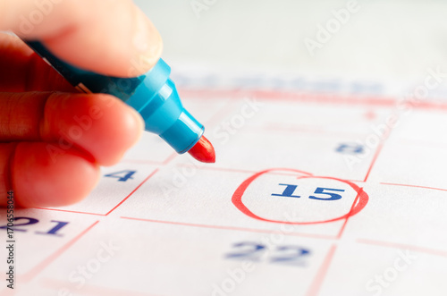 A female hand drawing a red circle with a marker on a calendar page. Business concept. 