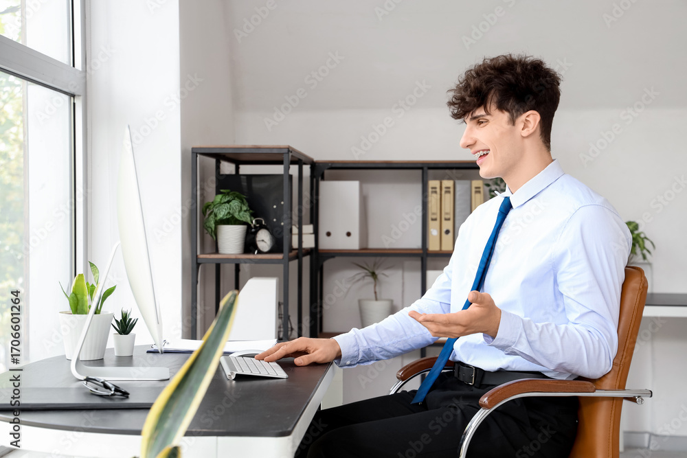 Fototapeta premium Young businessman with computer video chatting at table in office